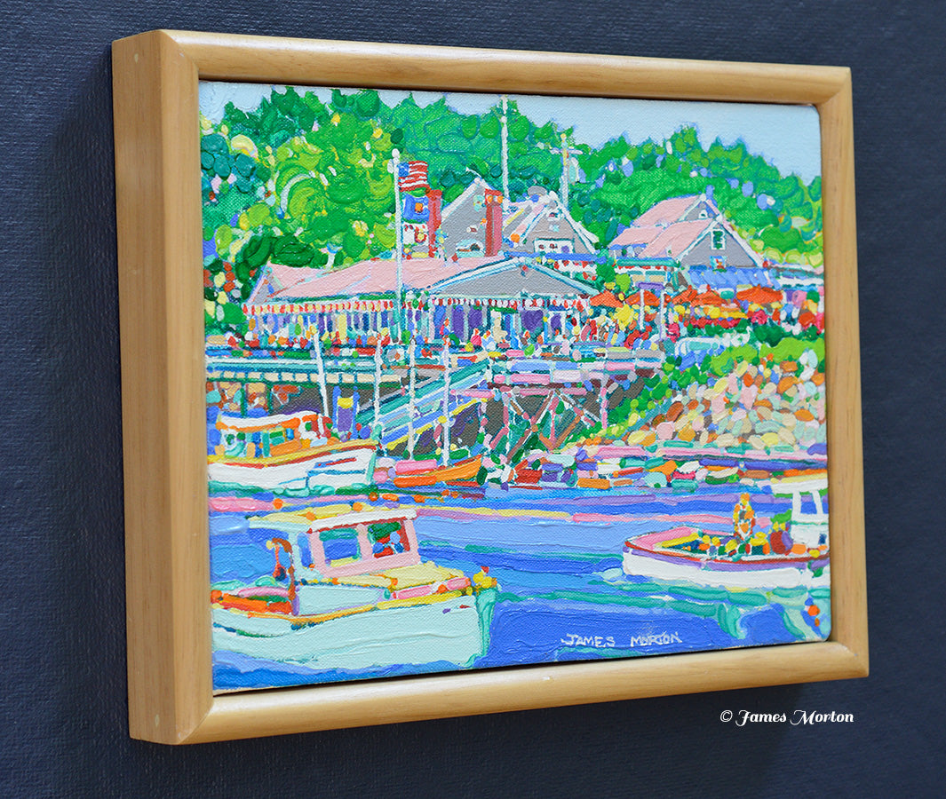 Left side angle view of a framed original Maine coastal painting depicting Barnacle Billy's restaurant at Perkins Cove in Ogunquit with fishing boats, blue harbor water, and surrounding green trees.