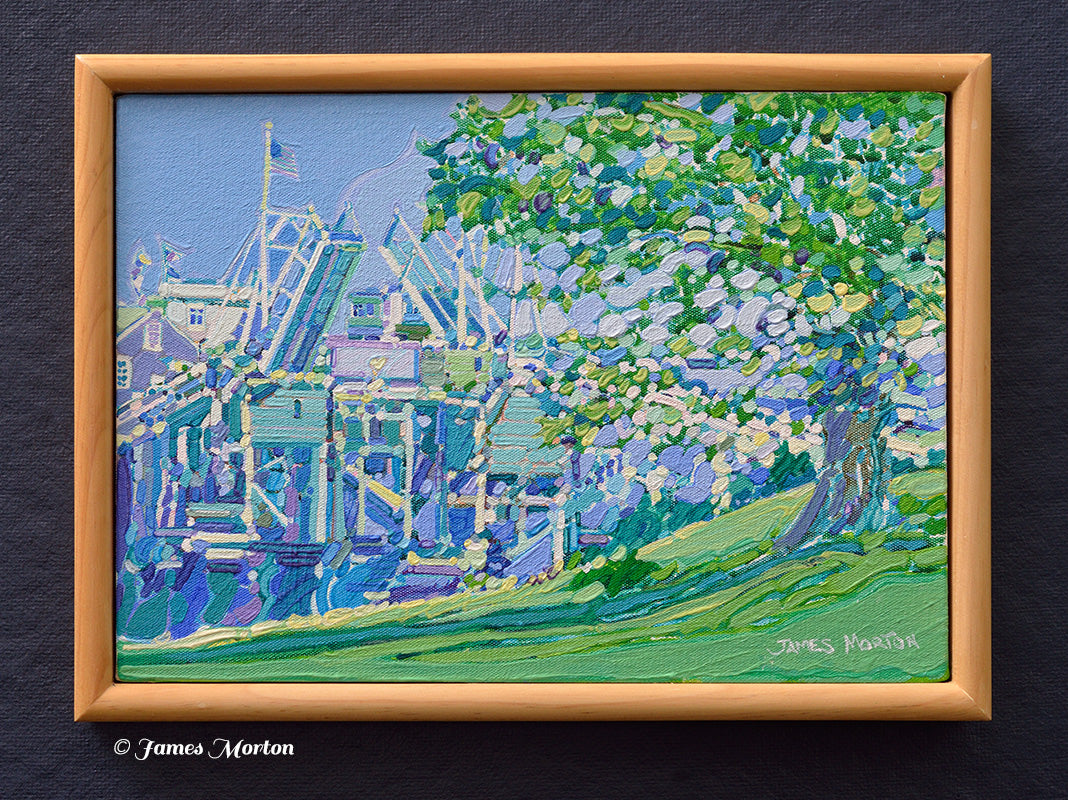 Original Ogunquit Maine painting of the Perkins Cove Drawbridge, framed in light wood. Impressionist acrylic painting featuring a coastal harbor scene with a large shade tree, green grass, and the artist's signature by James Morton.