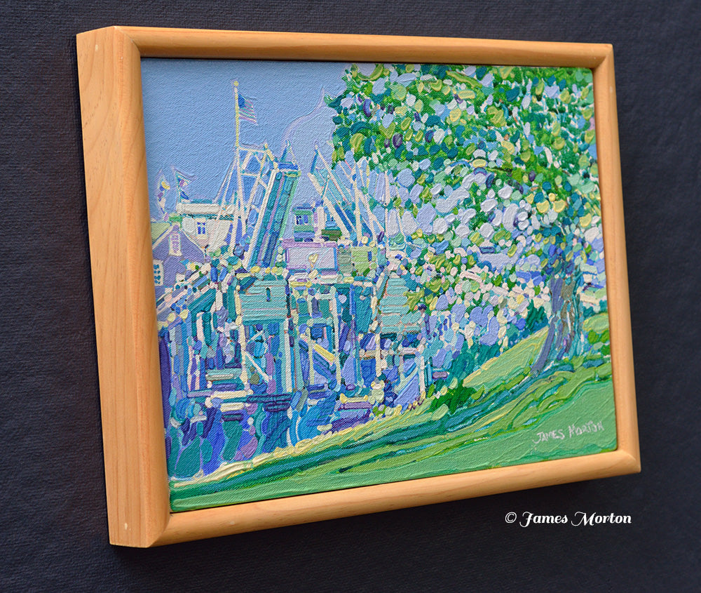 Left-side view of an original Perkins Cove painting in Ogunquit, Maine. Framed acrylic artwork depicting the historic drawbridge, coastal homes, green trees, and peaceful harbor landscape by James Morton.