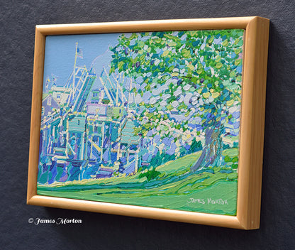 Right-side view of a framed original Perkins Cove painting in Ogunquit, Maine. Impressionist coastal artwork featuring the iconic drawbridge, vibrant green tree, blue harbor, and visible James Morton signature.