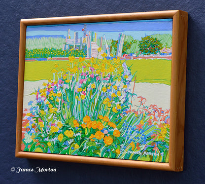 Right side view of the framed original Wellfleet, Massachusetts landscape painting, showing flowers in the foreground and a small boat dock in the background. The light brown pine wood frame and James Morton's signature near the bottom right of the artwork are visible.
