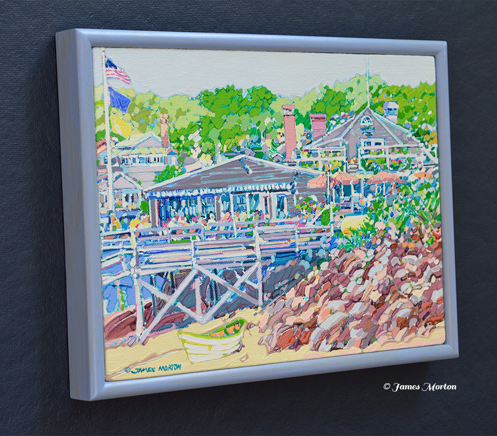 Left side angle view of a framed original Maine coastal painting featuring Barnacle Billy's restaurant at Perkins Cove in Ogunquit, with a sandy shoreline, small boat, rocky beach, and surrounding green trees.
