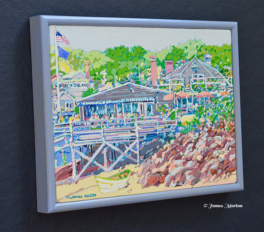 Left side angle view of a framed original Maine coastal painting featuring Barnacle Billy's restaurant at Perkins Cove in Ogunquit, with a sandy shoreline, small boat, rocky beach, and surrounding green trees.
