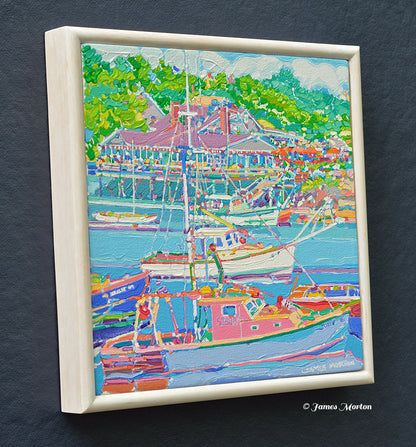 A framed original painting of Ogunquit Maine with fishing boats, green trees, and harbor side restaurant. The frame is white stained wood, and painted signature James Morton appears at the bottom right.