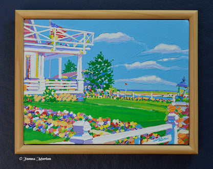 Framed original Ogunquit Maine acrylic painting depicting a classic New England Colonial inn with wrap-around porch, flower-lined garden path, lush green lawn, trees, and a distant Atlantic horizon along the Marginal Way. Artist signature by James Morton visible in the lower right corner.
