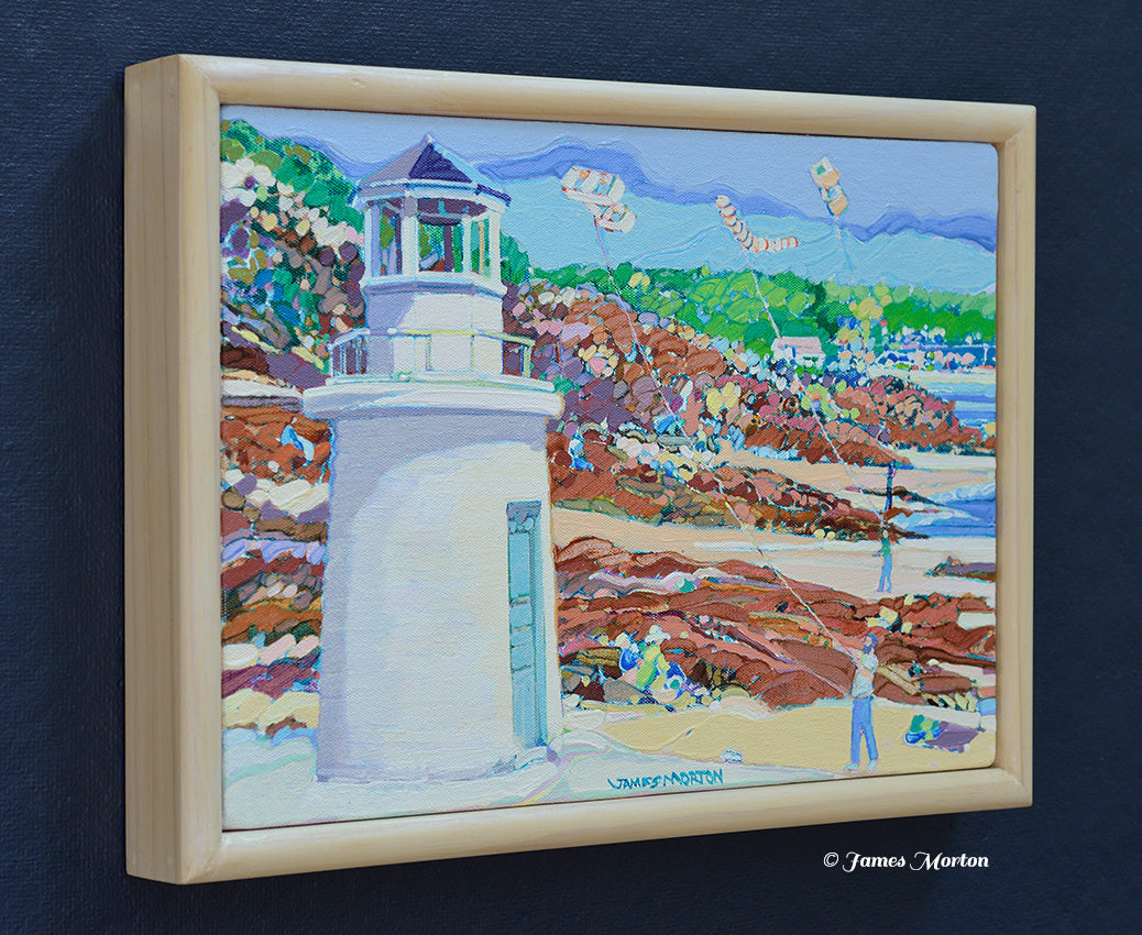 Left-angle view of a framed original coastal landscape painting featuring Lobster Point Lighthouse in Ogunquit, Maine, with rocky cliffs, ocean water, and the artist's signature visible on the lower middle.